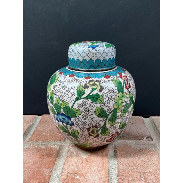 This antique handmade cloisonné lidded ginger jar features a brightly colored floral design against a white enamel...