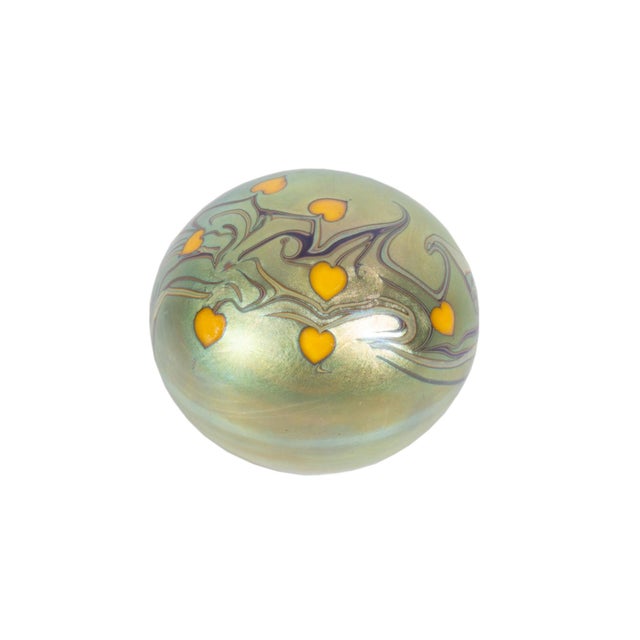 A 1975 iridescent art glass paperweight by Orient and Flume. This round paperweight features a swirling assortment of...