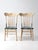 This charming pair of antique painted spindle back chairs features carved crest rails, floral detailing, and worn blue-...