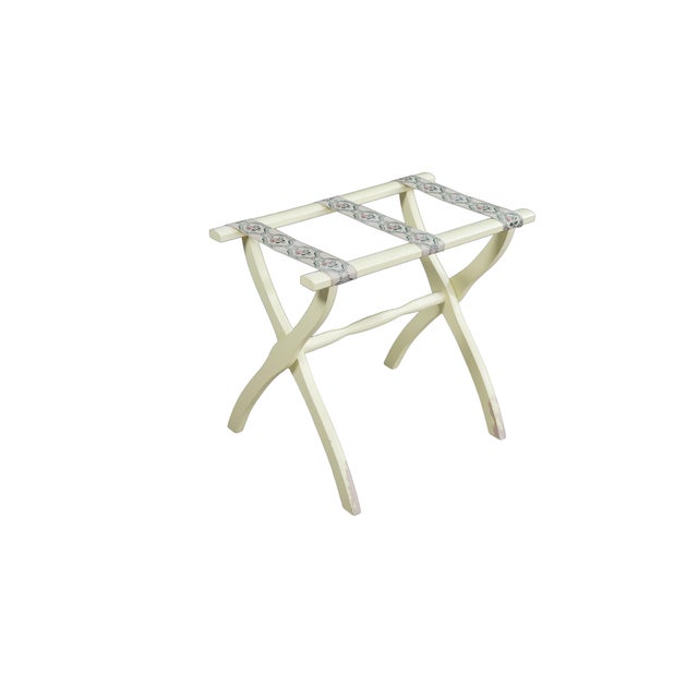 This vintage folding luggage rack features a classic scissor-frame design crafted from wood painted in a light cream or...