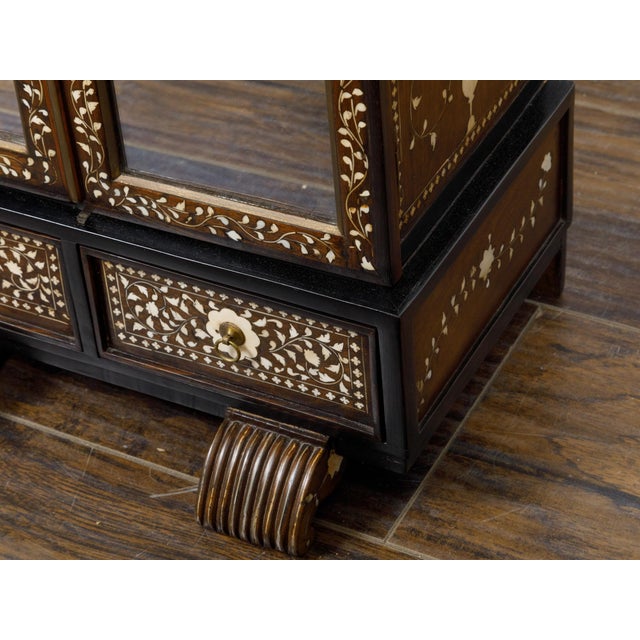 An English miniature cabinet from the 19th century with scrollwork inlay, glass doors and multiple inner drawers. This...