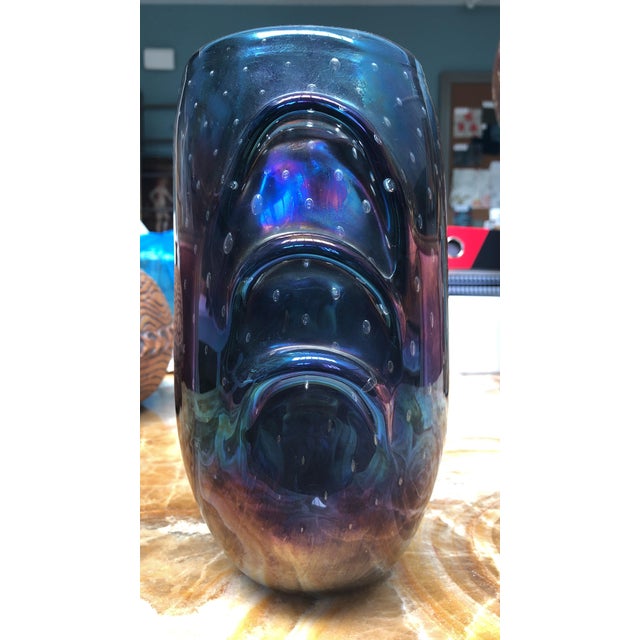 A dramatic hand-blown art glass vase featuring a deep, inky ground overlaid with a rich iridescent sheen that shifts...