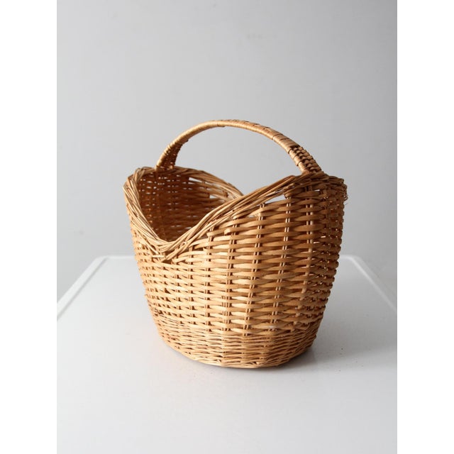 This vintage gathering basket features a softly curved form, arched handle, and warm woven surface that brings an easy,...