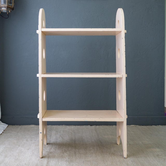 An antique handcrafted bucket bench turned bookshelf is painted in a pale peachy-pink tone, with a previous underlayer of...