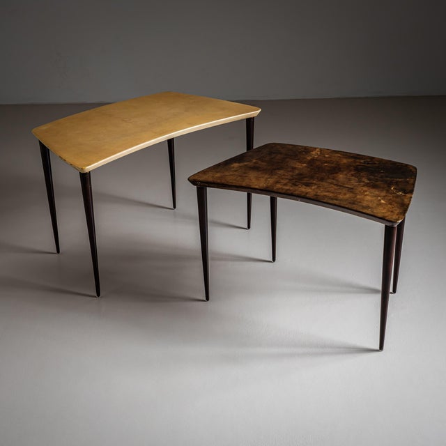 Two coffee tables by Aldo Tura featuring trapezoidal tops covered in goatskin parchment. The tables rest on ebonized...