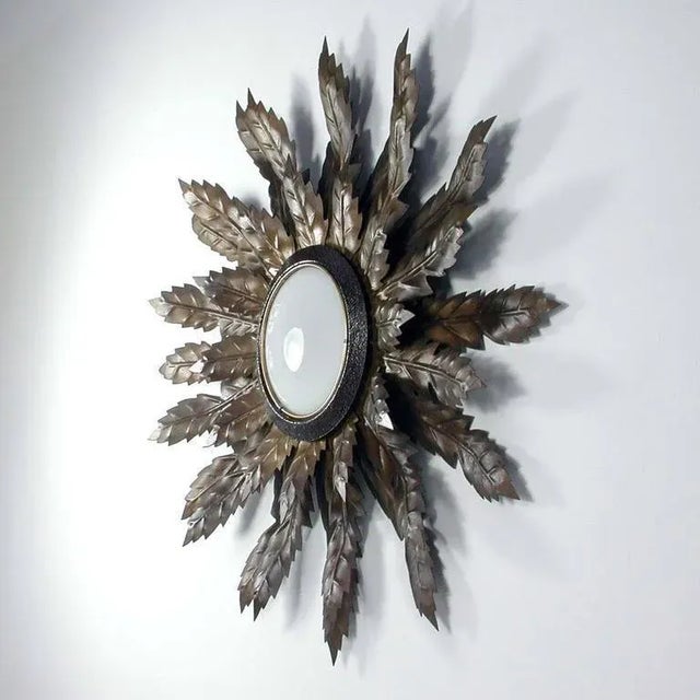 This Mid-Century sunburst sconce was produced in Spain in the 1950s. It is made of bronzed metal and has got a round opal...