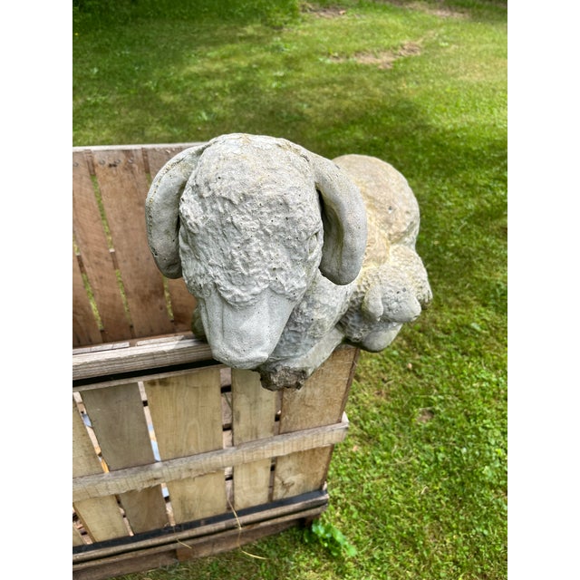 A single large cast concrete or cement garden statue of a sheep laying with a lamb.