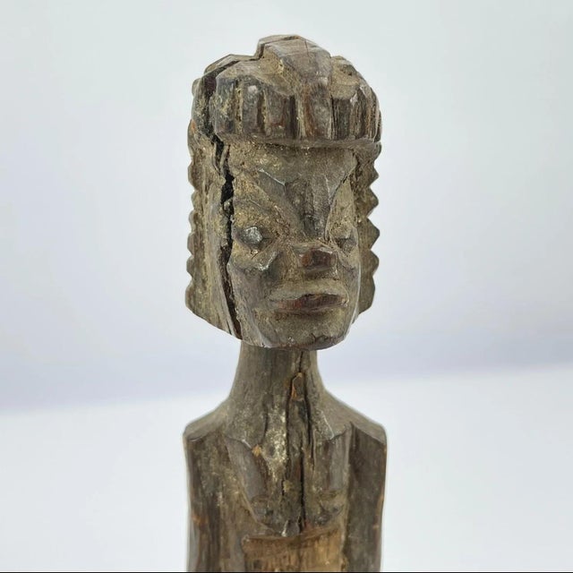 This carved wooden figure is attributed to the Tiv people of Nigeria. Standing in an upright, frontal pose with hands held...