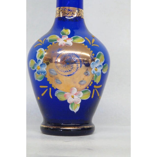 This lovely bud vase is made of glass. This piece features a gorgeous deep blue color to the glass with gilded gold...