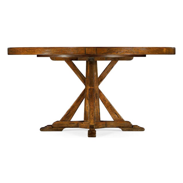 A round dining table finished in a warm walnut color with a rustic finish showing exposed saw marks and set on a bracketed...