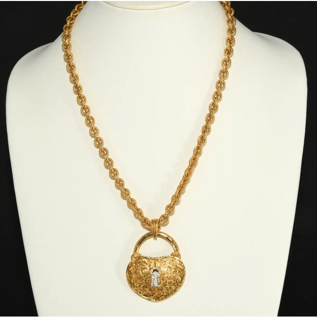 Heart shaped lock pendant with a keyhole outlined in clear rhinestones with textured chain. Metal is gold-plated. Marked...