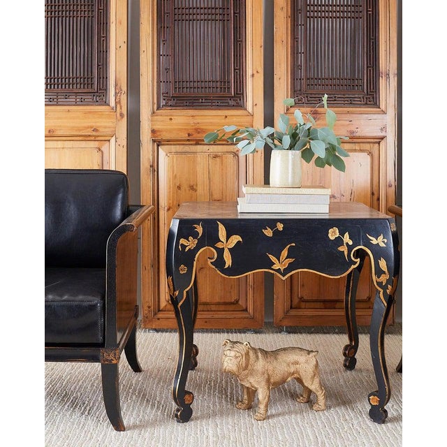 Dramatic black lacquered occasional or center table featuring a parcel gilt gold leaf chinoiserie decoration. This...