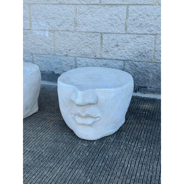 A pair of contemporary sculptural side tables featuring abstracted human faces carved in relief against substantial...
