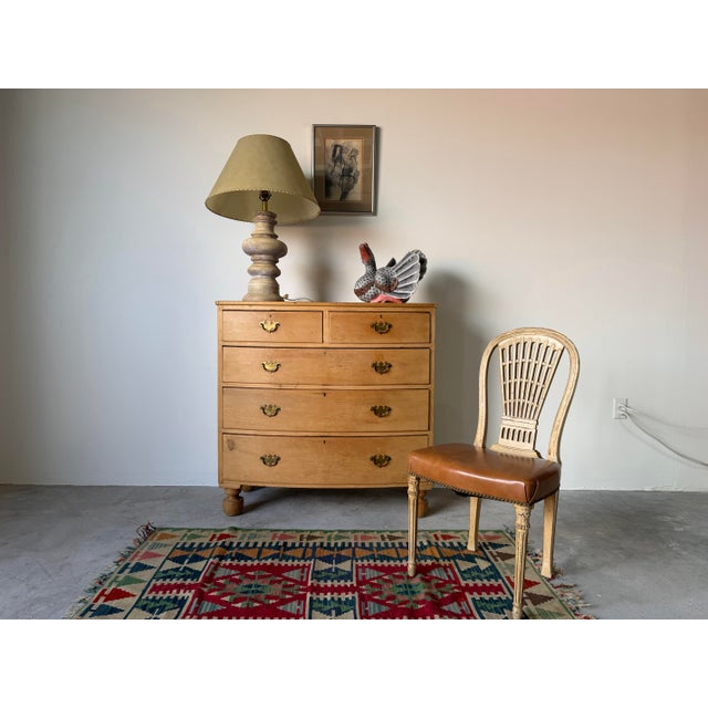 A beautiful antique 19th-century English pine chest of drawers featuring a graceful bow-front silhouette and warm honey-...