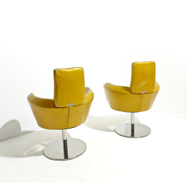Set of two swivel armchairs. Anatomically shaped leather/faux leather upholstery with chromed steel legs. Labeled by the...
