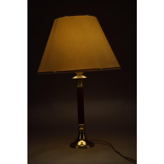 An elegant vintage brass table lamp with a rich burgundy column and a crisp white shade finished with subtle trim. The...