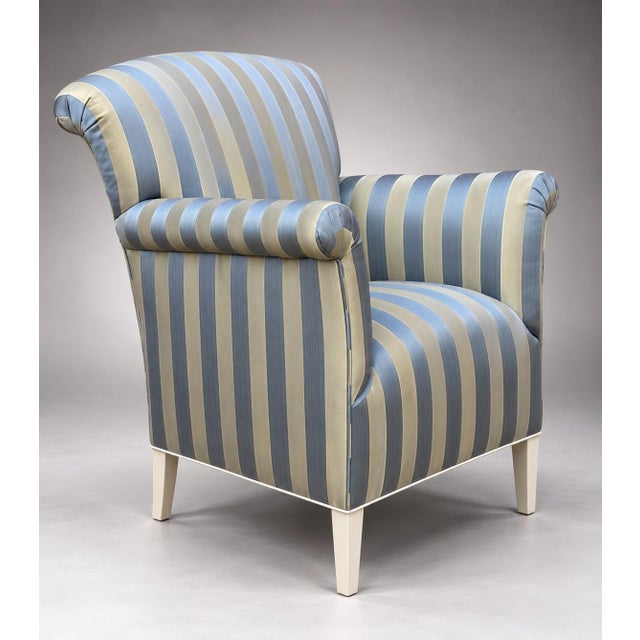 An upholstered lounge chair featuring rolled arms, a high curved back, and tapering wooden legs. The piece is covered in a...