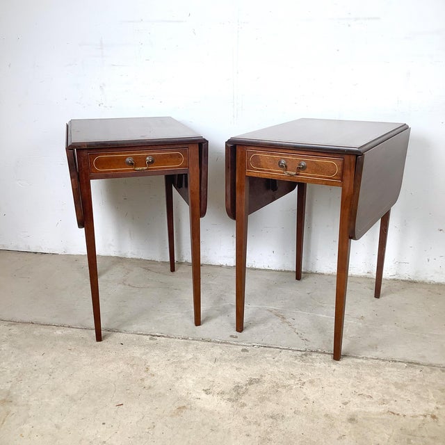 An elegant pair of Federal-style drop-leaf side tables featuring satinwood-style string inlay, single drawers with brass...