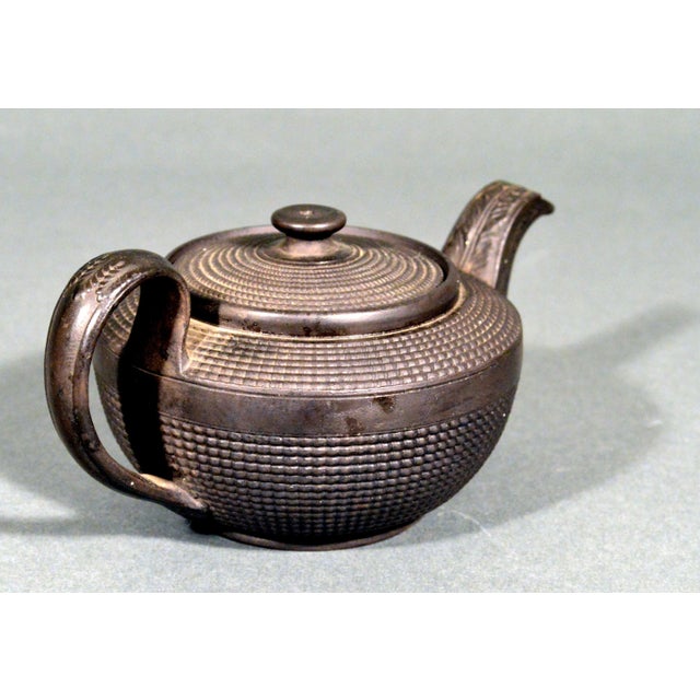 English Black Basalt Engine-Turned Teapot and Cover Circa 1790-1810 A compact and well-potted black basalt teapot of squat...