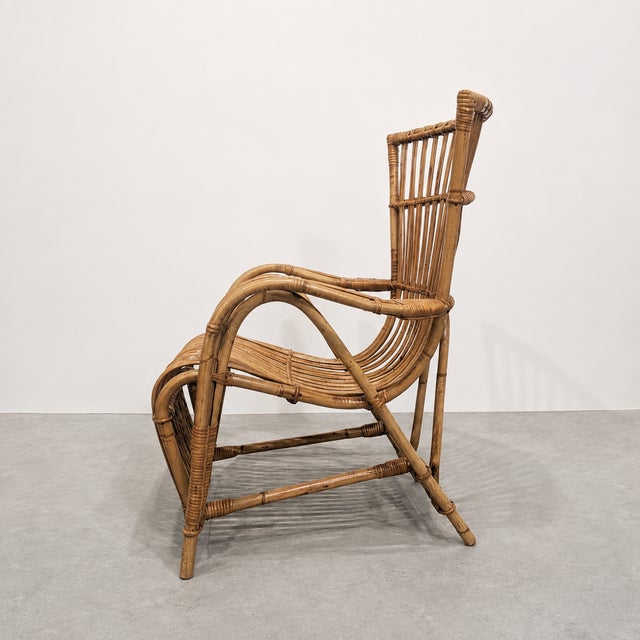 Vintage 1970s armchair crafted from natural rattan. The sculptural frame combines curved lines, enveloping armrests, a...