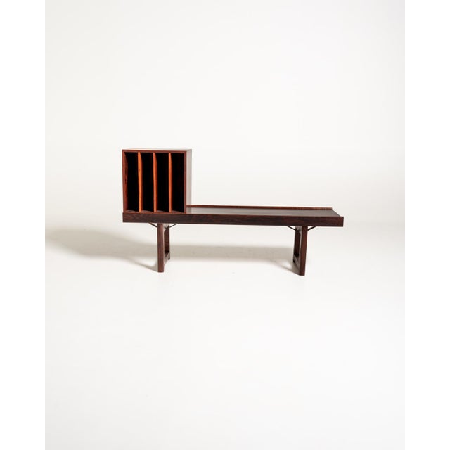Rosewood bench with a long, low top, frame legs, and a matching mobile record rack divided into four compartments. Made by...