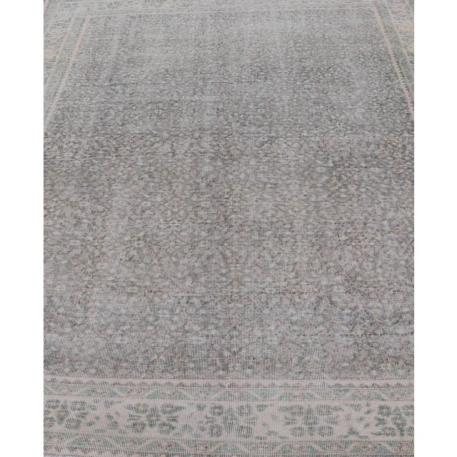 This vintage Turkish Oushak rug has been hand-knotted in wool and features an all-over sub-geometric distressed floral...