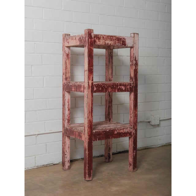 A sculptural wooden shelf whose presence is defined by an extraordinary, time-worn surface of deep red and chalky pink...