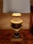 An elegant neoclassical-style table lamp crafted of carved wood with a rich black and deep mahogany-toned finish. Gilt...