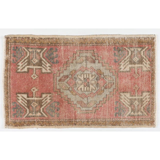 A vintage Turkish handwoven door mat rug featuring a bold geometric medallion and tribal motifs. Softly faded blush, sand,...