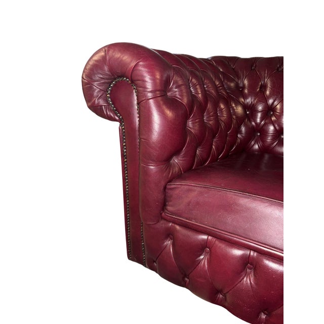 Classic English Chesterfield armchair upholstered in burgundy leather, featuring deep diamond button tufting, rolled arms,...