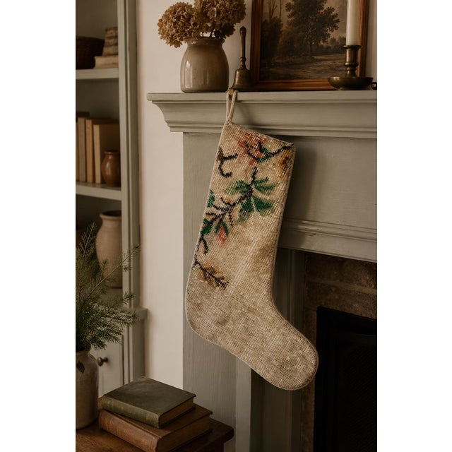 This vintage wool kilim stocking features a charming hand-woven botanical branch motif in soft coral, sage green, and tan...