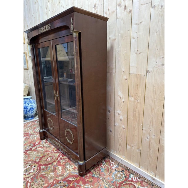 A two-door Empire-style bookcase/display cabinet in solid and veneered mahogany. The upper section consists of two glazed...