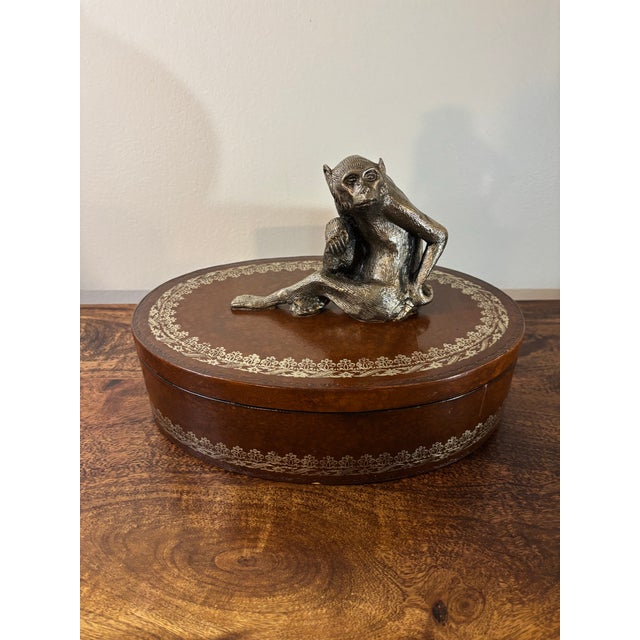 A distinctive vintage leather decorative box attributed to Maitland Smith, featuring a sculptural cast metal monkey finial...