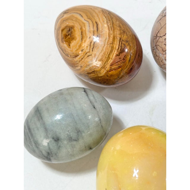 Set of five solid stone decorative eggs with polished surfaces and varied natural veining and banding. Colors range from...