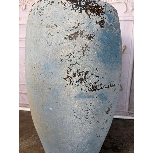 A beautifully proportioned terracotta vessel distinguished by its soft, rounded silhouette and heavily weathered pale blue...