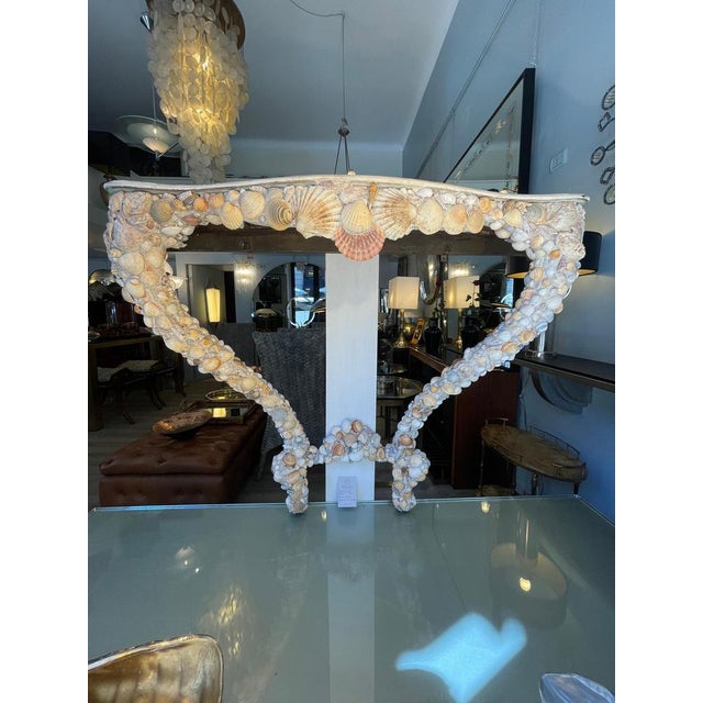 A handcrafted 1950s Venetian-style console table featuring a wooden frame covered with various types of seashells. This...
