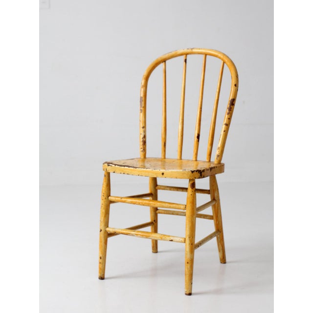 This antique Windsor-style chair features a classic rounded bow back, slender turned spindles, and a warm mustard-yellow...