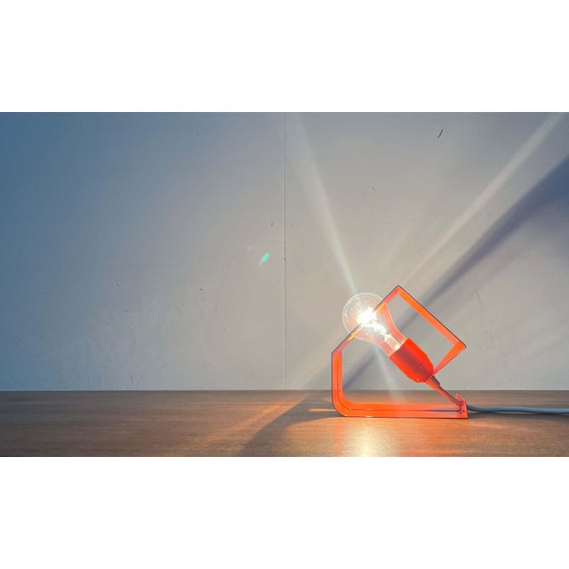 Minimalist Space Age table lamp in orange. The design impresses with its simple, cubic forms. The lamp body is a folded...