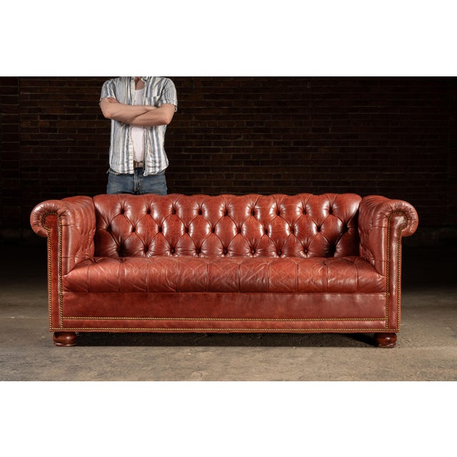 A handsome vintage Chesterfield sofa upholstered in richly colored burnt-red leather. The classic silhouette features a...