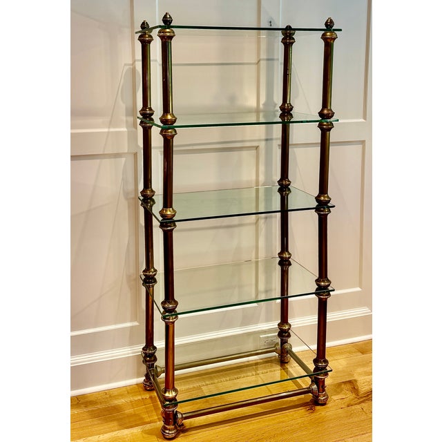 A striking mid-century brass and glass étagère featuring five substantial glass shelves suspended within a framework of...