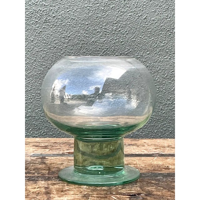 This vintage green pedestal glass vase, likely dating to the mid-20th century, pairs a softly rounded bowl with a...