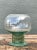 This vintage green pedestal glass vase, likely dating to the mid-20th century, pairs a softly rounded bowl with a...