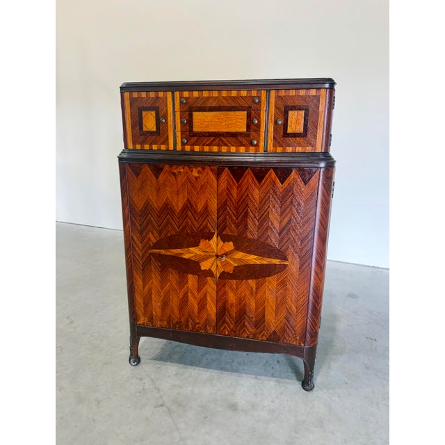 Detailed marquetry adorns the front of this handsome 1930’s Art Deco tall dresser or Chiffonier. Chevron Inlays across the...