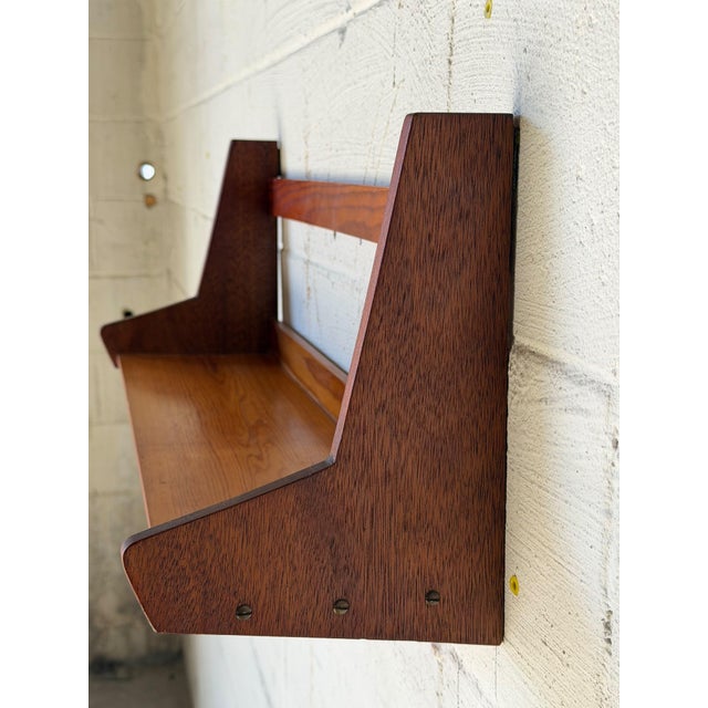 Beautiful vintage Danish modern wall-mounted shelf featuring sculptural wooden side supports, a warm wood finish, and...