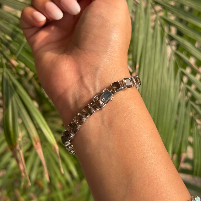 This elegant tennis bracelet is crafted in 925 solid silver and set with 24 cushion-cut smoky quartz gemstones, each...