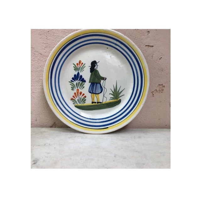 A French large faience plate with a farmer in the costume with flowers signed Henriot Quimper, circa 1950. Colorful yellow...