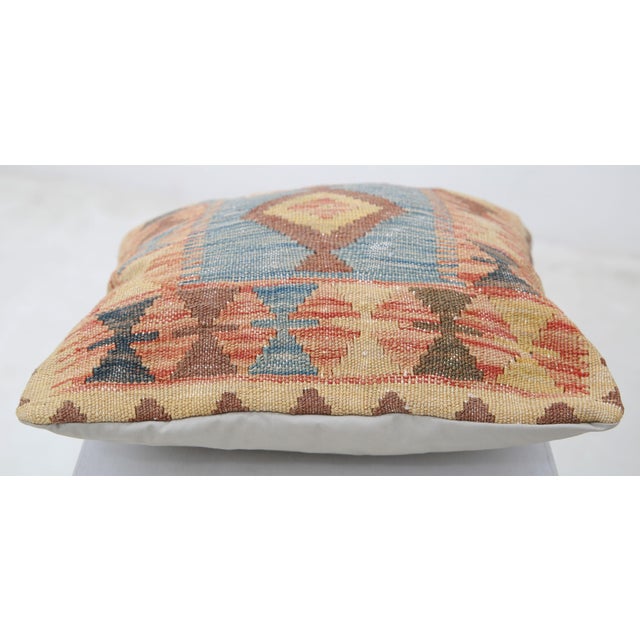 A one-of-a-kind handwoven Afghan wool kilim accent pillow featuring blue center panel with a diamond and bowtie border....