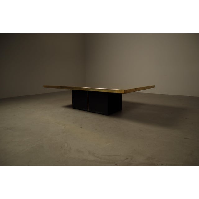 The table features a rectangular wooden top clad with an etched brass plate, resting on a black lacquered metal base with...