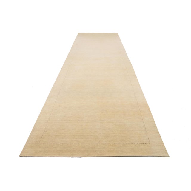 This hand-crafted wool rug, styled in Gabbeh fashion, features a minimalist pattern with blue and brown accents on a beige...