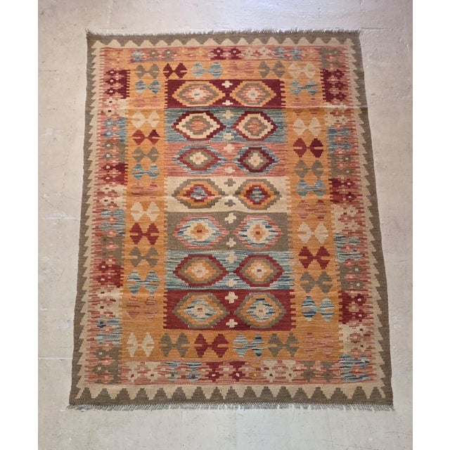 vintage Afghan Maimana kilim rug featuring bold tribal geometric patterns and a warm, earthy color palette. Handwoven with...
